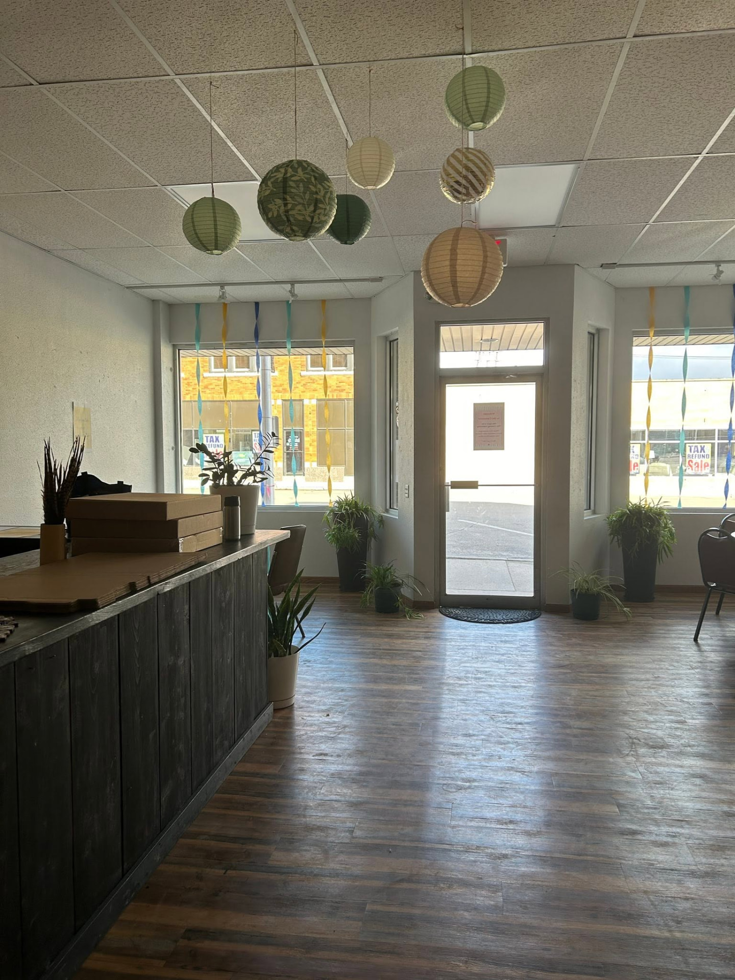 Inside The Commons on Main in Rugby, ND: the front door and storefront windows, wood floor, plants and hanging paper lanterns
